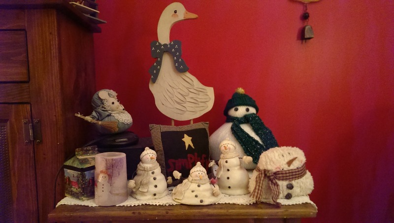 A collection of ceramic and knitted snowmen near to candles in the windows.