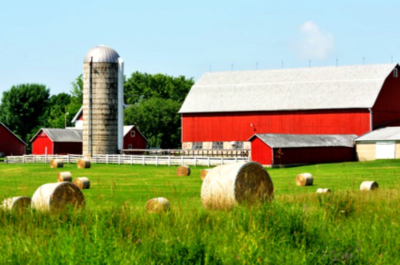 Pretty red barn with silver silo and round bales of hay in the field